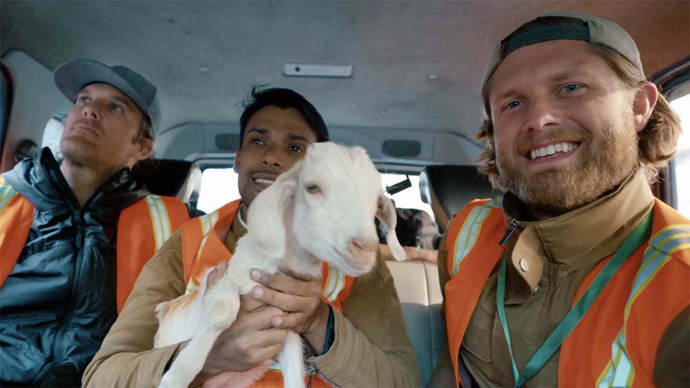 Three men, center man holds goat