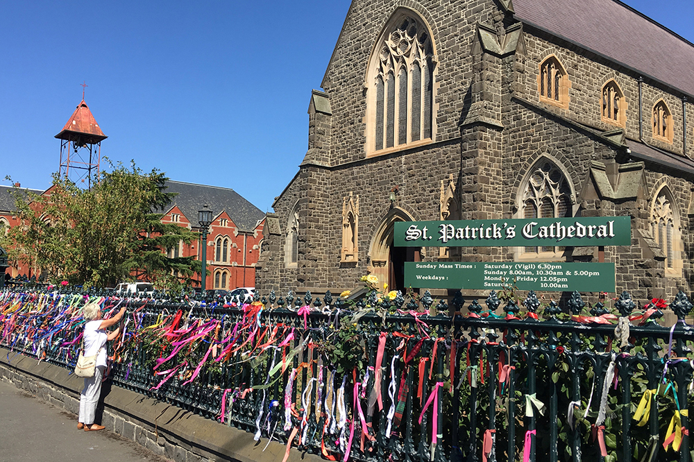 A woman puts a ribbon on the fence of St. Patrick's Cathedral in Ballarat, Australia, Feb. 27, 2019. The ribbons raise awareness and show support for victims of abuse. (CNS/Reuters/Jonathan Barrett)