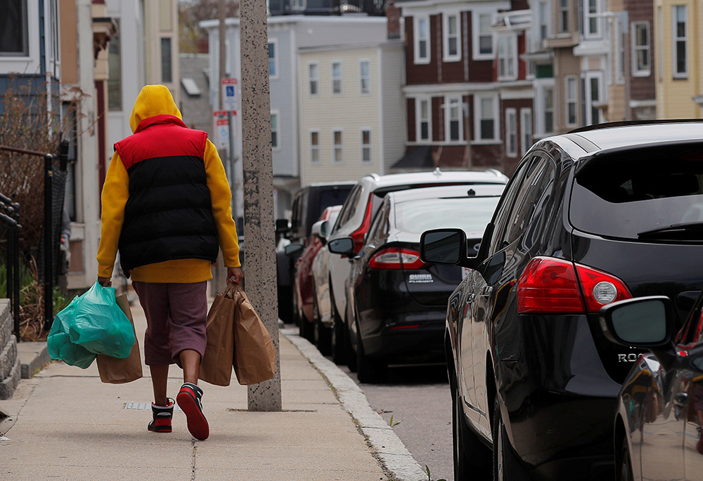 A woman walks away with free groceries from a food pantry and free hot meals from a church in Boston April 14, 2020. Poverty is among more than a dozen issues covered by a new Vatican document on human dignity. Dignitas Infinita ("Infinite Dignity") was released April 8, by the Vatican's Dicastery for the Doctrine of the Faith. (OSV News/Reuters/Brian Snyder)