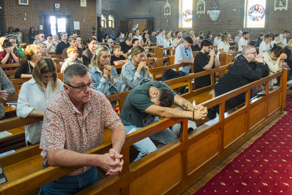 Faithful kneel in pews, praying the rosary.