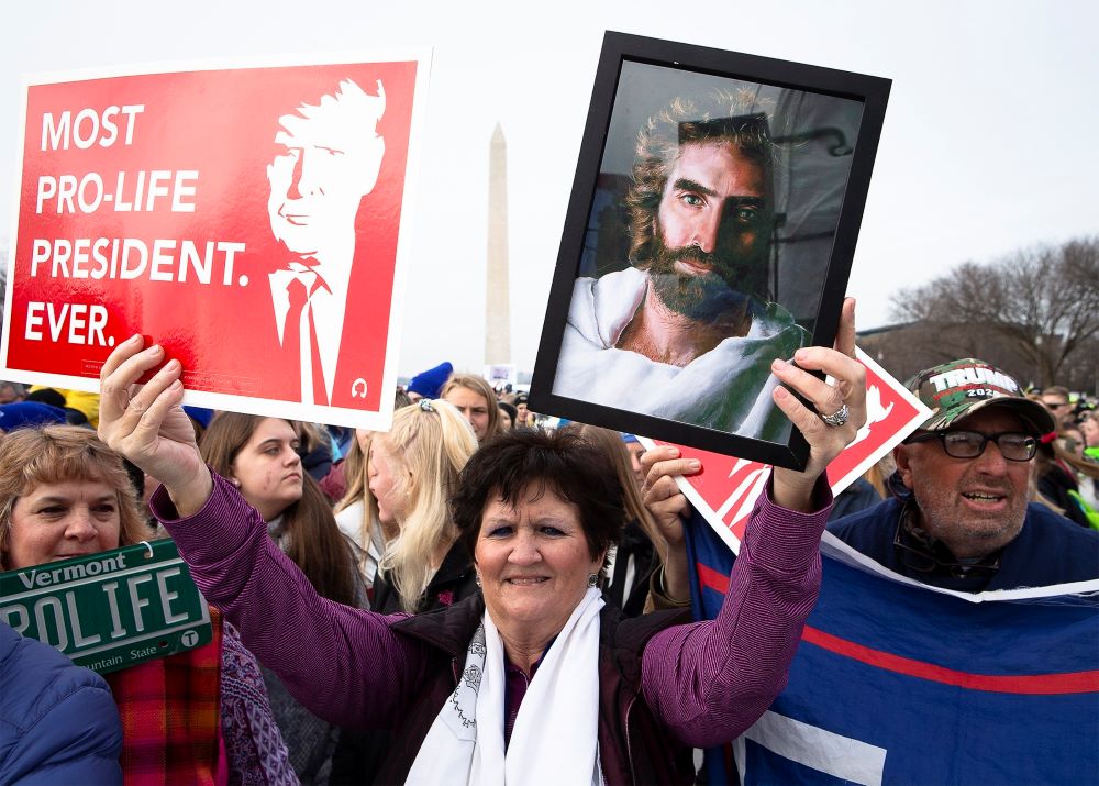 A woman holds an image of Jesus and a poster about President Donald J. Trump during the annual March for Life rally in Washington Jan. 24, 2020. 