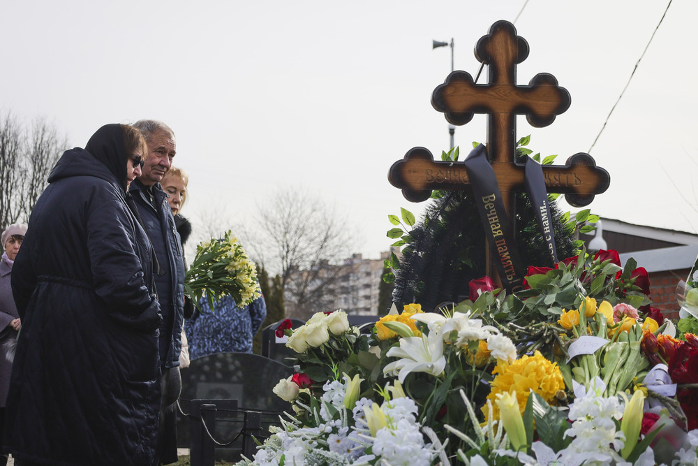 People gather outdoors around cross bedecked with flowers