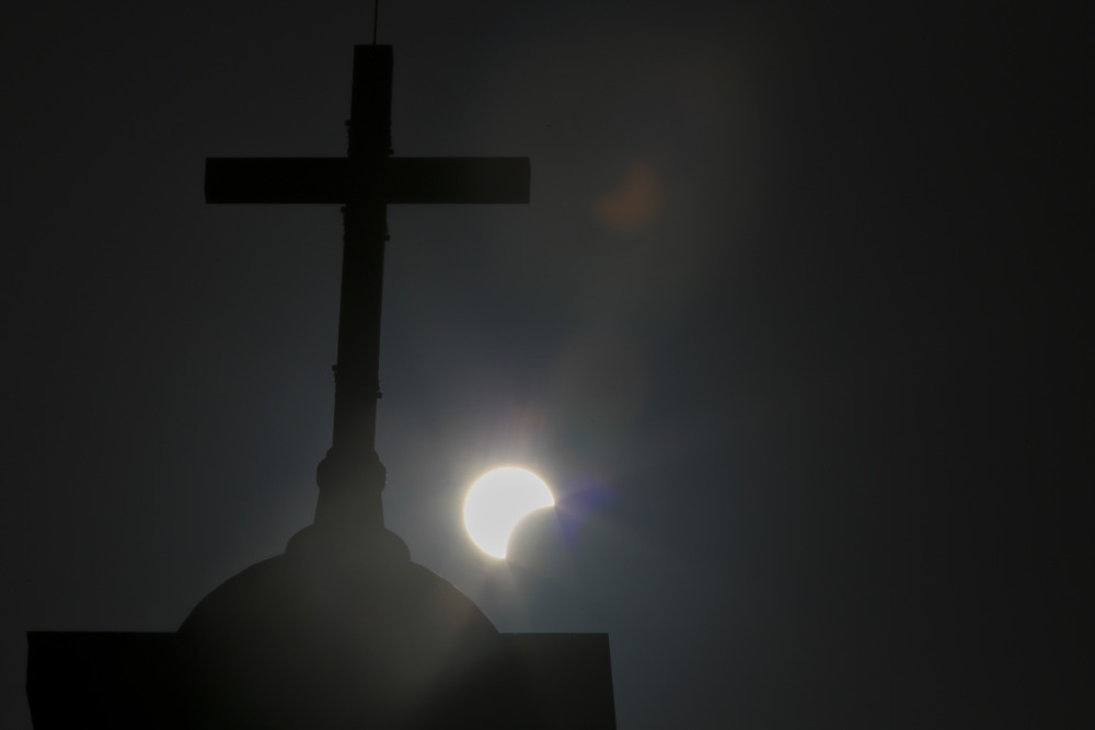 Cross silhouetted against eclipsing sun