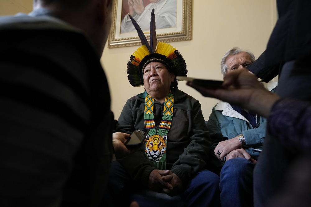 Man wearing traditional Amazonian garb sits while fielding questions