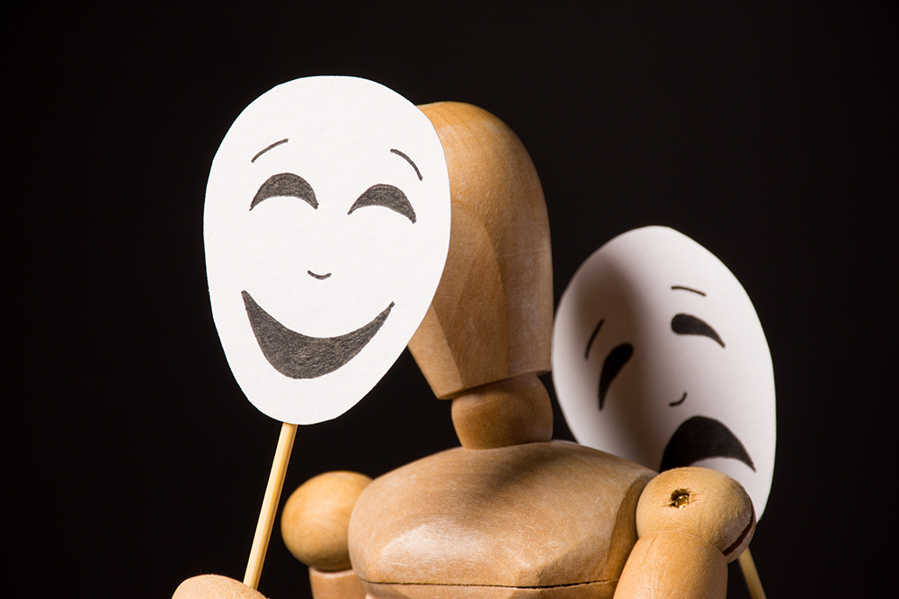 Wooden human figure holds a happy mask and a sad mask (Dreamstime/Oksana Volina)