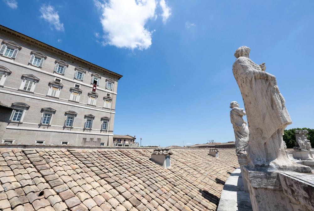 Statues and roof in foreground, and in distance Pope Francis' window with banner. 