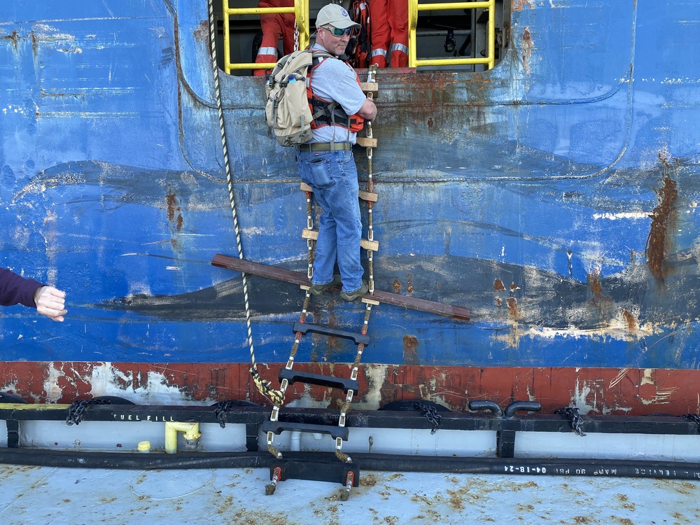 Middleton, on ladder wearing backpack, turns to look at camera. 