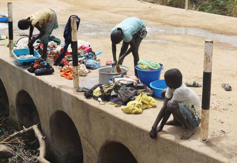 Uganda, gender based violence. Children bend or squat with buckets to wash laundry.