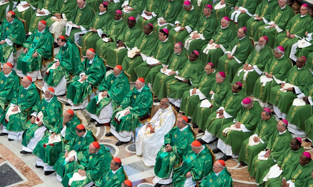 Synod of Bishops on young people, faith, and vocational discernment Bishops, vested for Ordinary Time, sit in vast assembly pictured from above.