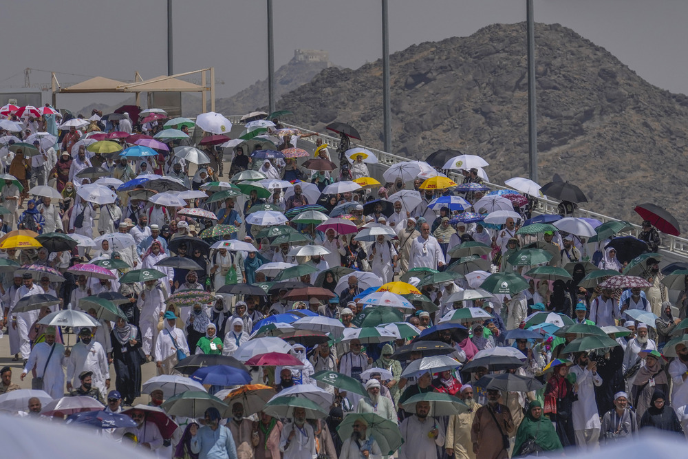 Hajj deaths 2024 Large crowd pictured under their umbrellas against mountainous, desert terrain.