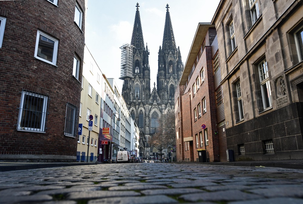 German Catholic Church exodus Cathedral of Cologne, one spire obscured by scaffolding, looms over cobblestone street.