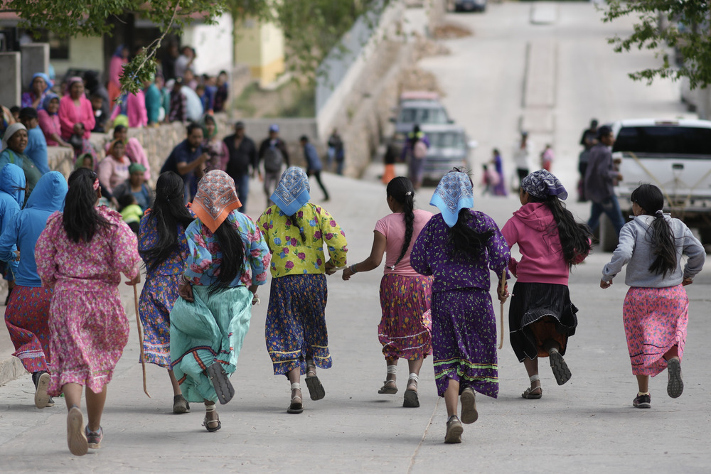 Raramuris Women wearing brightly colored skirts and headscarves, pictures from behind, running through street.
