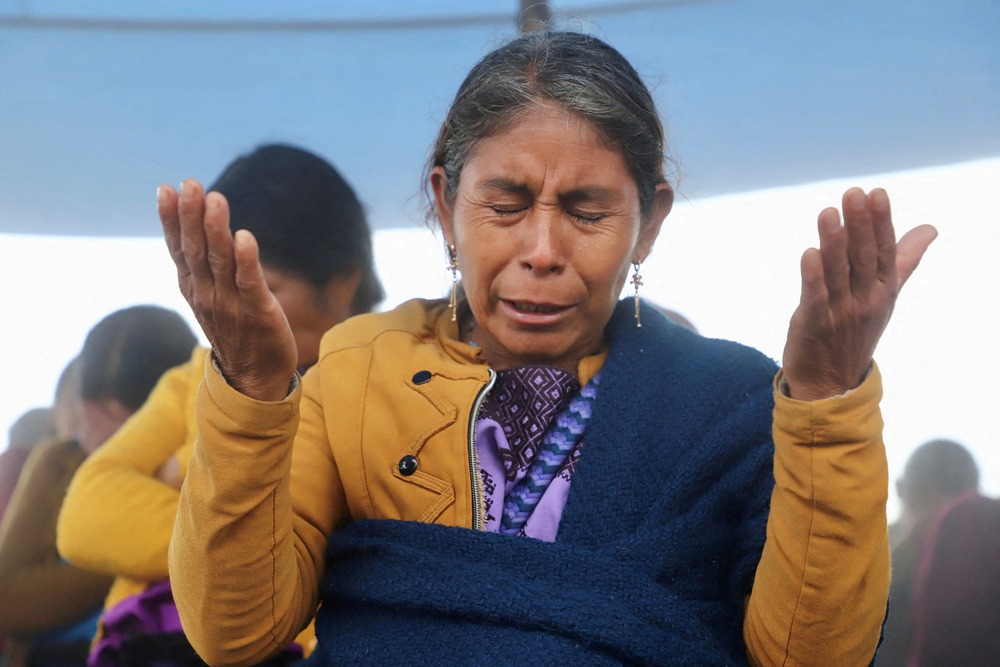 Tzotzil Indigenous woman, Chiapas, Mexico, 2022. Woman holds hands up, and bows head in prayer.
