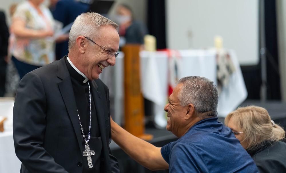 Bishop Zarama of Raleigh North Carolina at the 2024 Tekakwitha Conference Zarama smiles as a conferece attendee laughs and affectionately touches his arm.