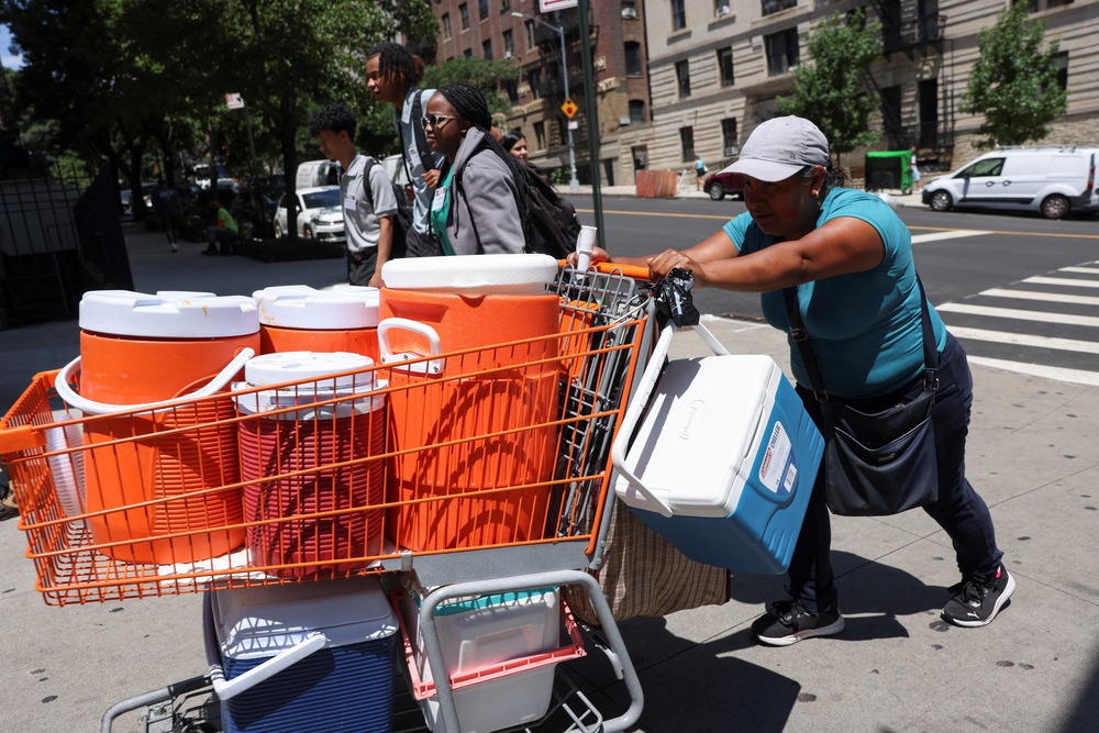 Record breaking summer temperatures, 2024. Woman pushes shopping cart filled with large coolers.