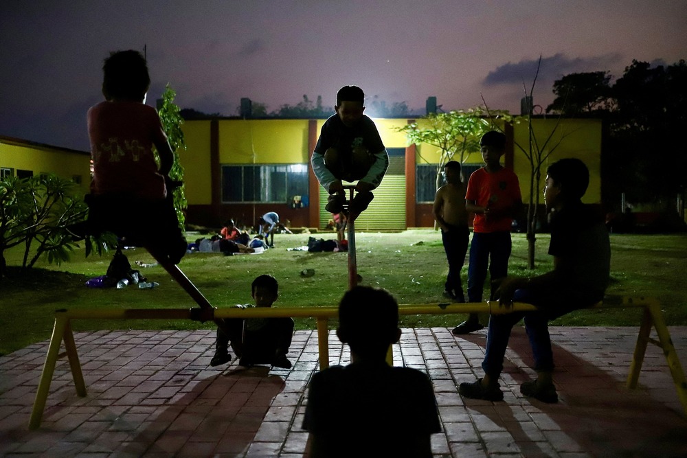 A school in Los Corazones, Oaxaca state, Mexico, 2024. Kids ride a see-saw at night, floodlights light background.
