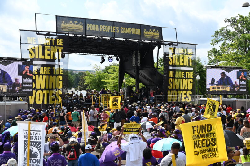 Poor People's Campaign rally June 29 Large assemble holding sign, and a large platform bearing banners that read "the silent swing vote".