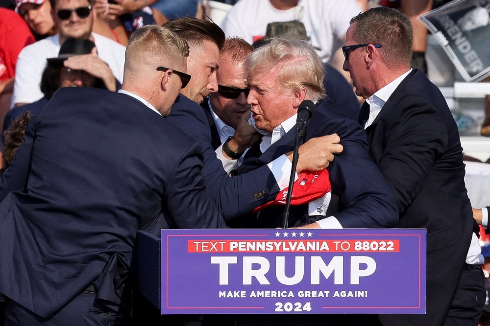 Republican presidential candidate and former U.S. President Donald Trump is assisted by guards during a campaign rally after shots were reportedly fired at the Butler Farm Show in Pennsylvania July 13, 2024. A local prosecutor says the suspected gunman and at least one attendee are dead.