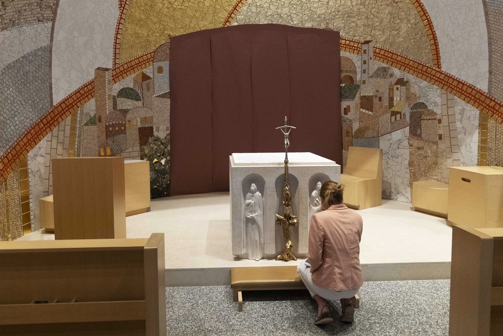 Knights of Columbus, Washington D.C shrine, Luminous Mysteries Chapel with Rupnik's mosaics, 2024. Woman kneels at small altar, behind altar are Rupnik's mosaics.