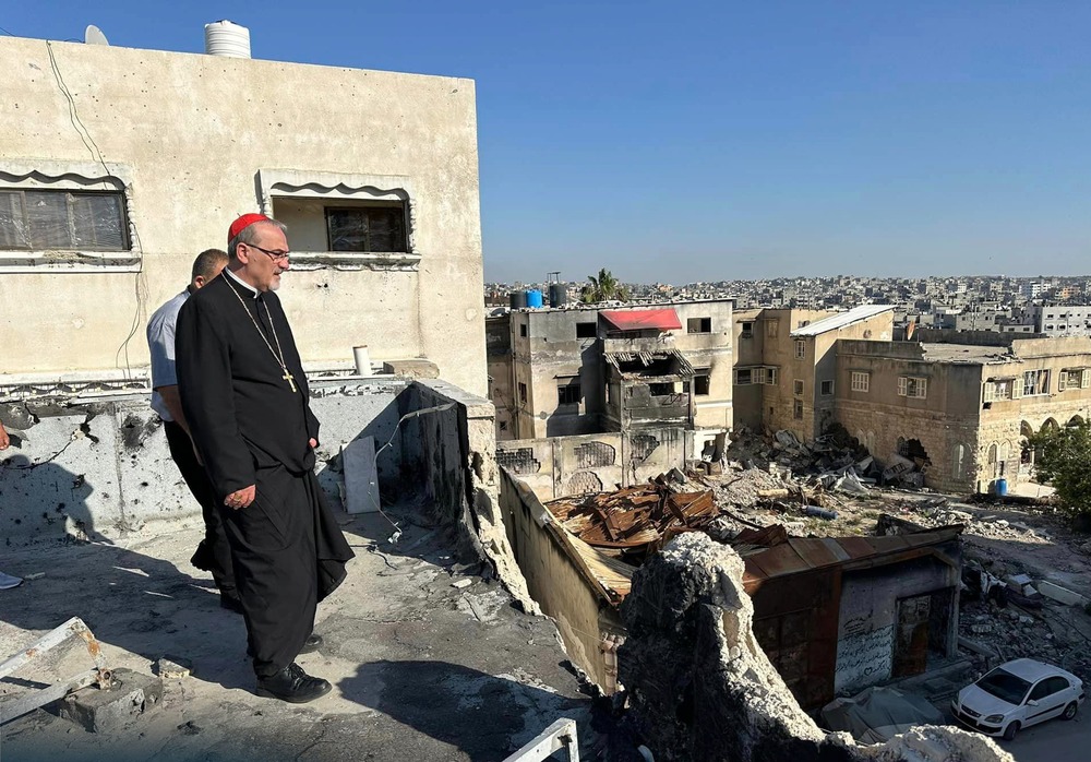 Cardinal Pierbattista Pizzaballa, the Latin patriarch of Jerusalem, walks through the ruins of buildings in Gaza City; May, 2024. Pizzaballa stands on rooftop surveying vast ruins; the cardinal wears plain black clericals, with a red zucchetto.