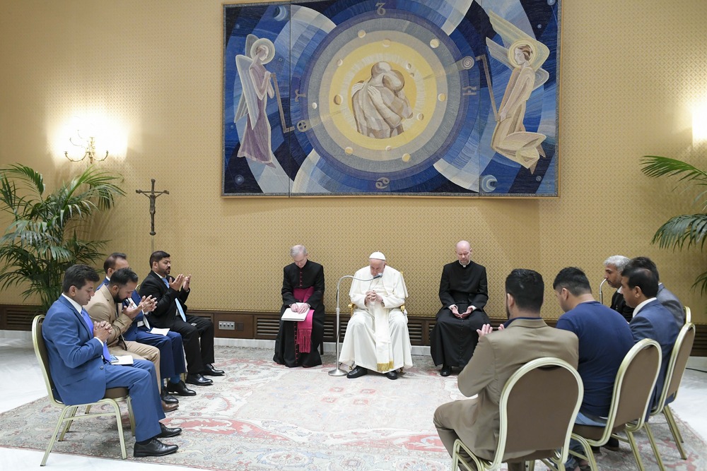 Pope Francis meeting with members of the Afghan Community Association in Italy; Paul VI Hall, Vatican City, Aug. 7, 2024. Francis seated, flanked by prelates, seated in circle around pope are association representatives.