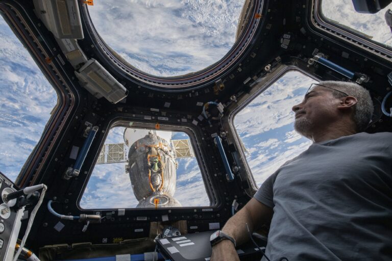 Astronaut in spacecraft looks out window at earth.