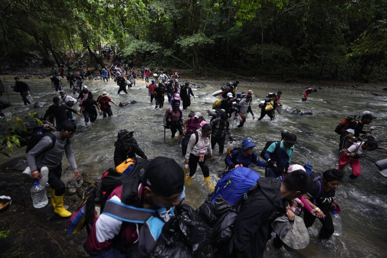 Migrants crossing Darien Gap, Oct. 15, 2022. People wearing backpacks and other burdens walk through running water in jungle terrain.