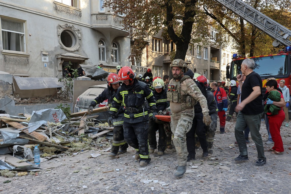 Aftermath of Russian airstrike on Lviv, Ukraine, Sept. 4, 2024. Decimated street, covered in rubble; uniformed emergency workers carry stretcher through wreckage.