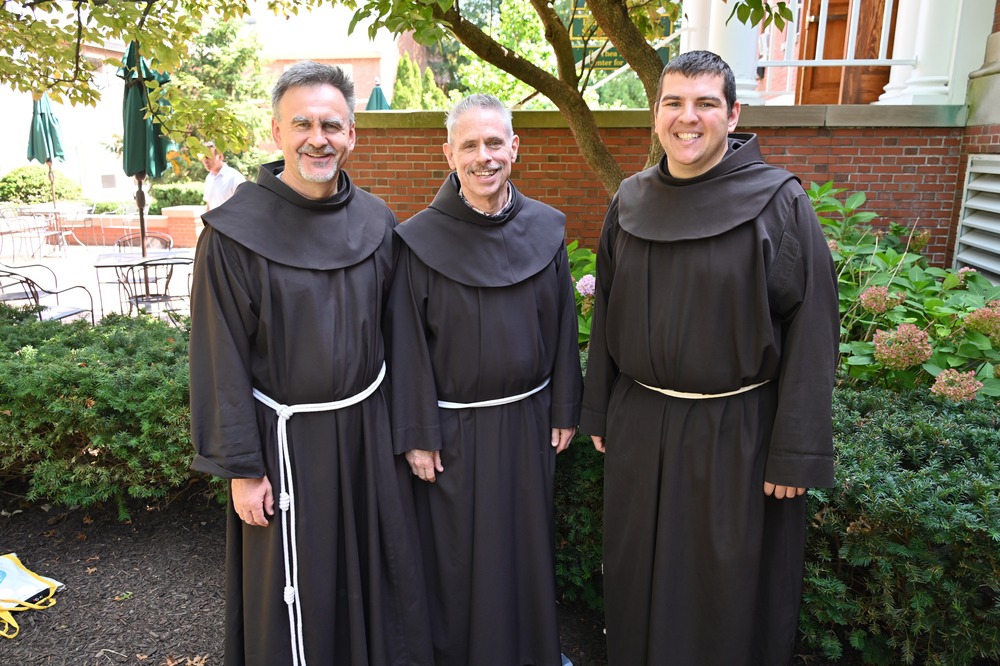 Franciscan Bros. Jacek Orzechowski, Michael Perry and Jimmy Kernan. The three friars stand under a tree smiling.