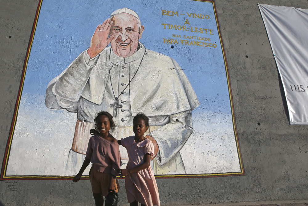 Pope Francis trip, East Timor, 2024. Two young children stand beneath large mural of Pope Francis.
