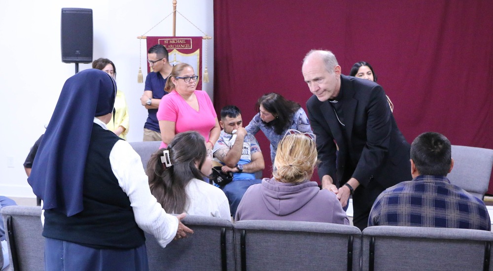 Bishop Mark Beckman of Knoxville, Tennessee, upper East Tennessee, Oct. 2, 2024. People sit and stand, some crying. The bishop bends down to shake a hand.