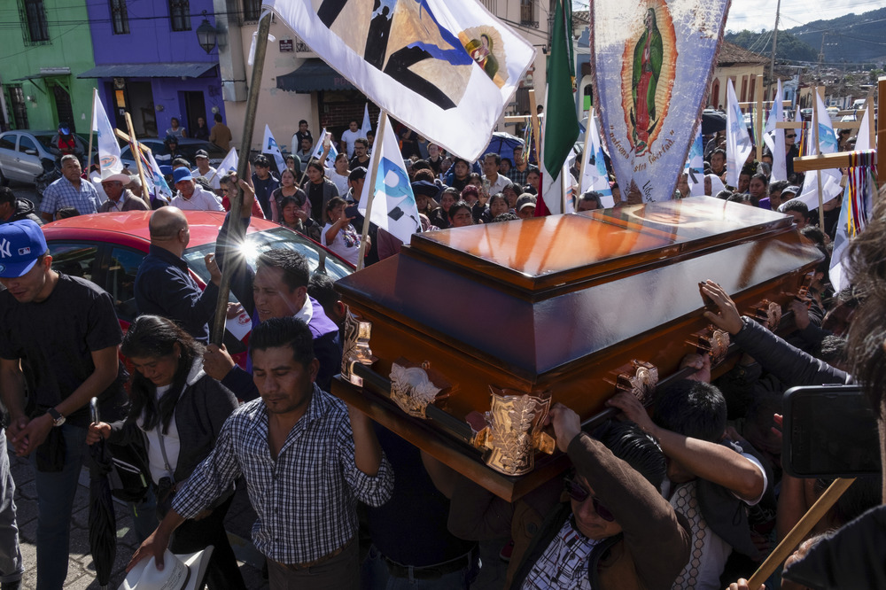 Funeral procession of Fr. Marcelo Perez, Chiapas State, Mexico, 2024. Pall-bearers carry casket, surrounded by large group carrying banners and votives.