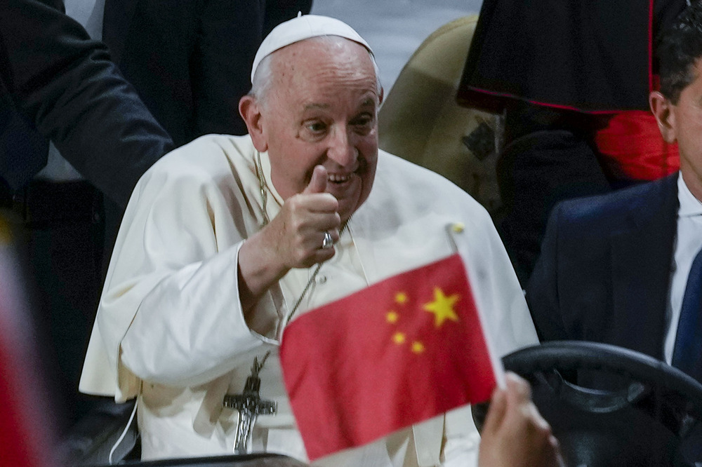 Pope Francis, Mongolia, Sept. 3, 2023. Francis smiles and gives thumbs up, foregrounded is small, hand-held Chinese flag.