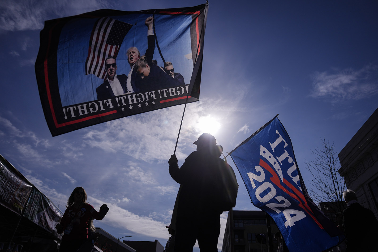 Trump rally, Allentown, Pa., Oct. 29, 2024. People holding Trump flags silhouetted against bright sun.