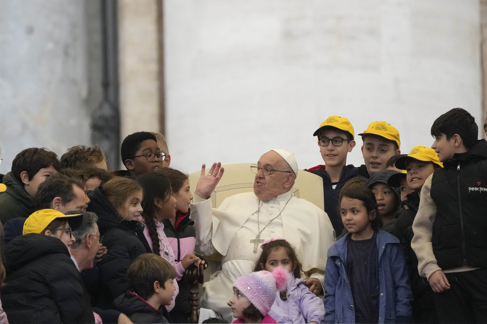 Pope Francis with children during general audience, Nov. 20, 2024. Pope sits surrounded by children; he gestures and smiles, wearing glasses.