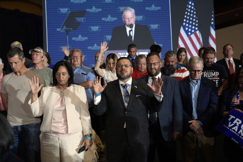 Franklin Graham, Trump rally, North Carolina, Oct. 21, 2024. People stand with their hands raised, behind is a projector screen showing Graham.