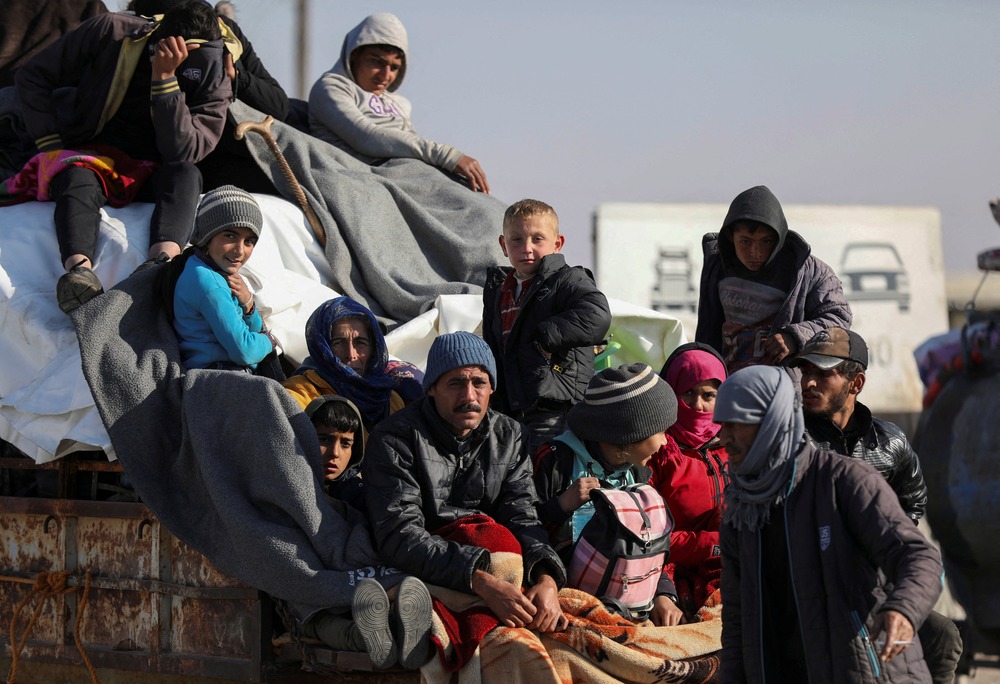 Displace Syrians, Tabqa, Syria, Dec. 3, 2024. Adults and children, bundled up and carrying items, sit on back of vehicle.