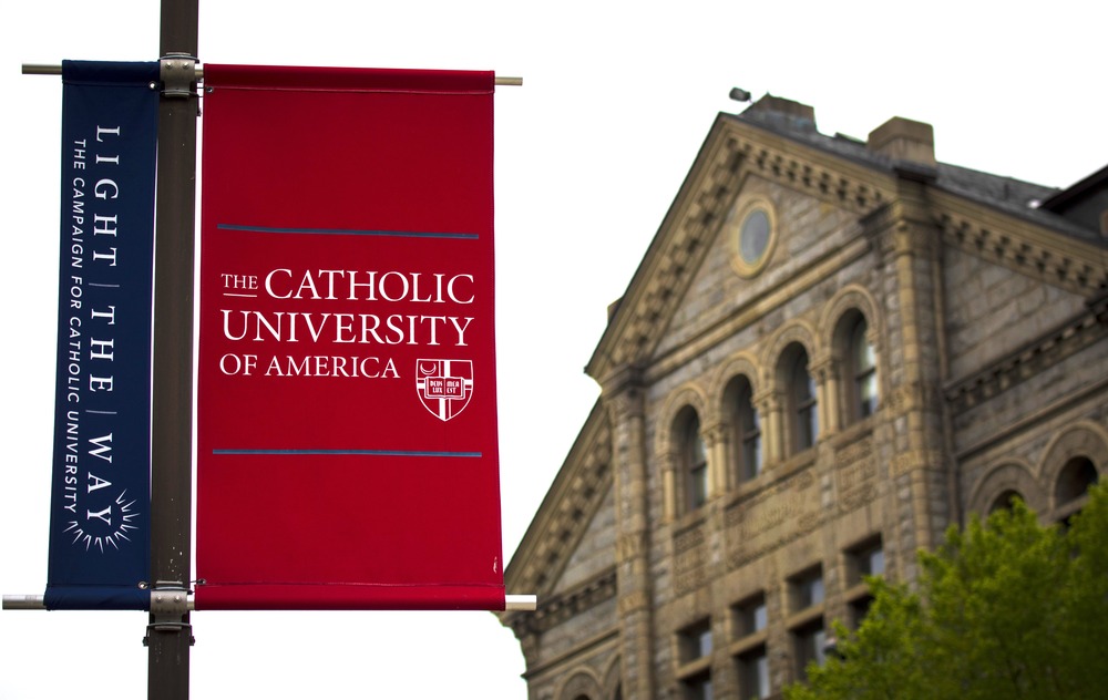 Washington campus of the Catholic University of America, May. 18, 2020. Banner foregrounded, stone building in background.