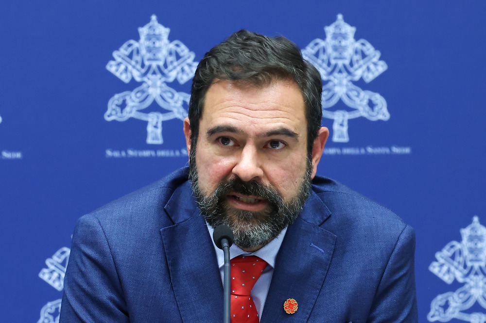 Victor Genina Cervantes, director of integral human development at Caritas Internationalis, Vatican Dec. 23, 2024. Cervantes pictured sitting at press conference wearing blue suit and red tie.