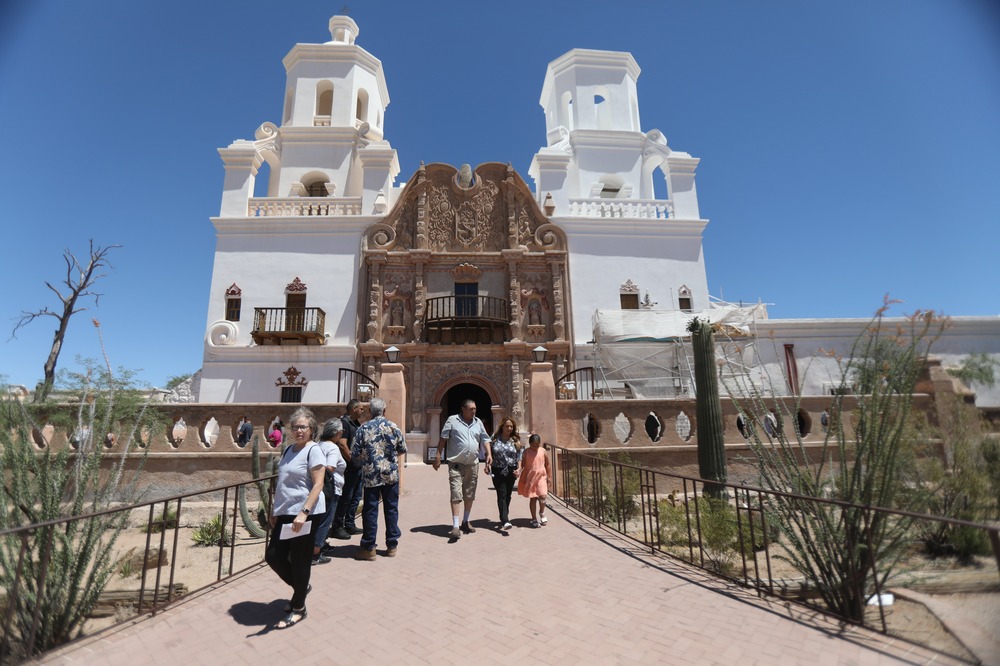 San Xavier del Bac Mission, Pima County, Ariz., May 28, 2023. People walk out of large mission style church.
