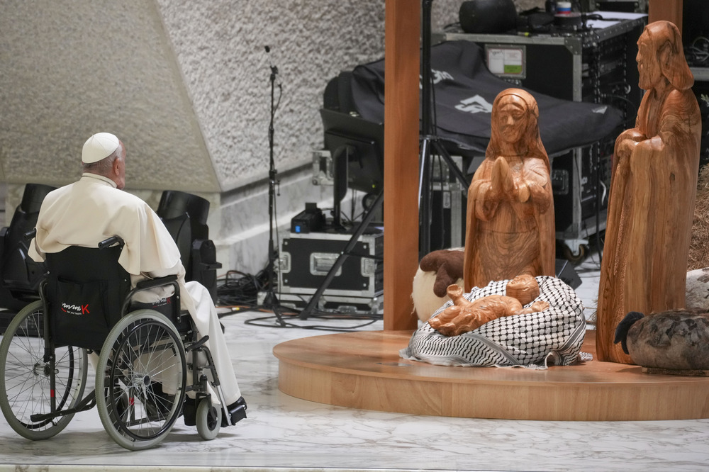 Pope Francis, Vatican, Dec. 7, 2024. Pope Francis in wheelchair sits before wooden nativity scene with keffiyeh.