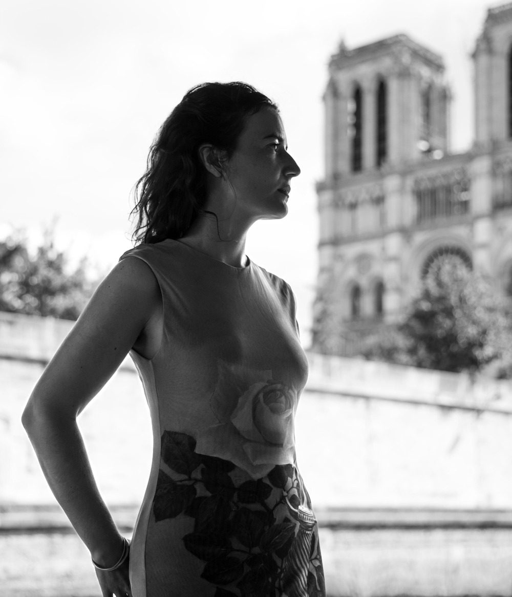 Lise Borel, French composer affiliated with Notre Dame de Paris. Black and white portrait of Borel standing in front of Notre Dame de Pari.