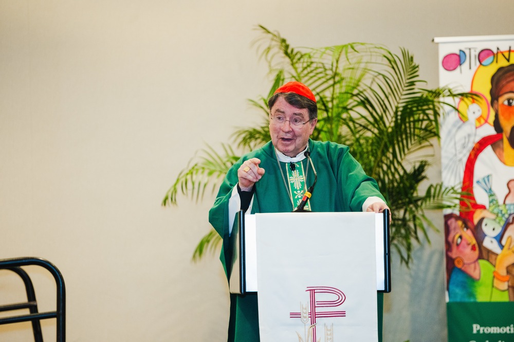 Cardinal Pierre vested for ordinary time stands at ambo gesturing and speaking.