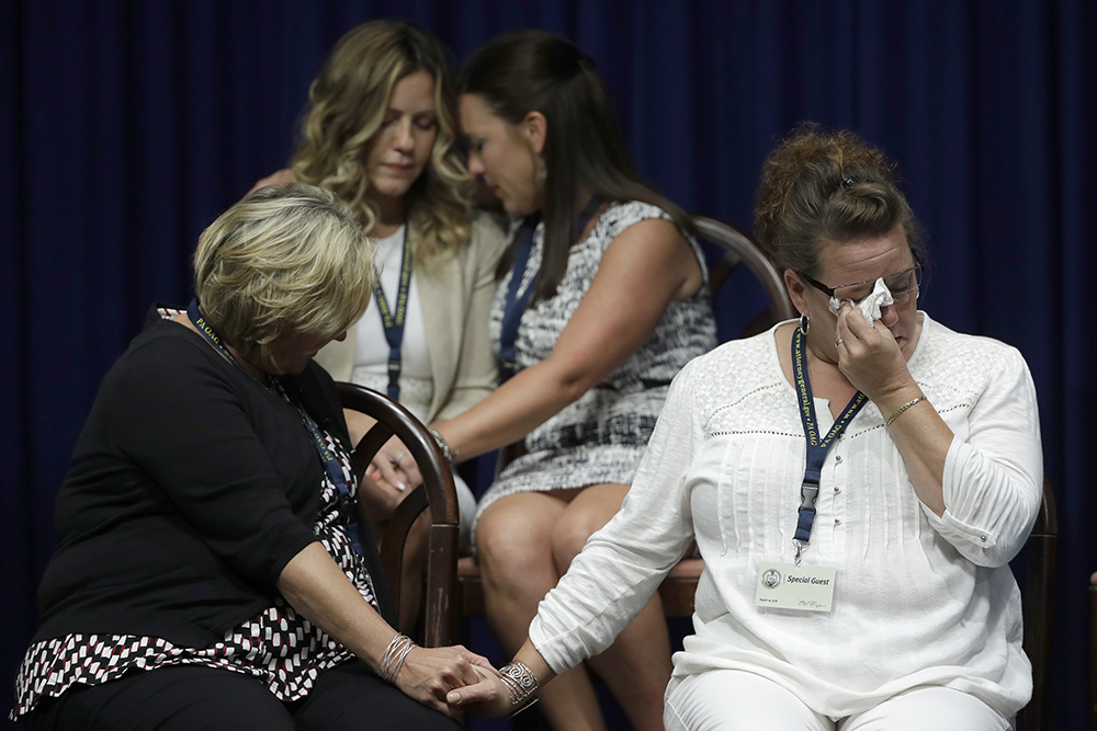 Church sex abuse press conference, Harrisburg, Pennsylvania, Aug. 14, 2018. Four women sit while dabbing tears and holding hands.