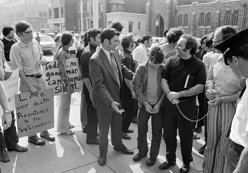 Supporters of persons arrested a week earlier in an attempted raid on a Selective Service office greet those arrested at a court hearing in Camden, New Jersey, on Aug. 30, 1971. Those arrested were brought from a New Jersey jail in handcuffs. Among them is John Grady, right, handcuffed, wearing black. They became known as the "Camden 28." (AP photo/Bill Ingraham)