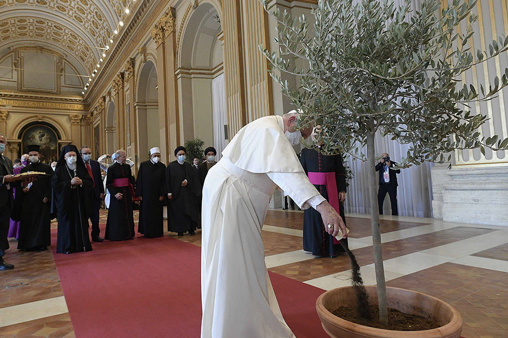 Pope Francis pours dirt into a potted olive tree during the meeting, “Faith and Science: Towards COP26,” with religious leaders in the Hall of Benedictions at the Vatican Oct. 4, 2021. The meeting was part of the run-up to the U.N. Climate Change Conference, called COP26, in Glasgow, Scotland, Oct. 31 to Nov. 12, 2021. (CNS/Vatican Media)