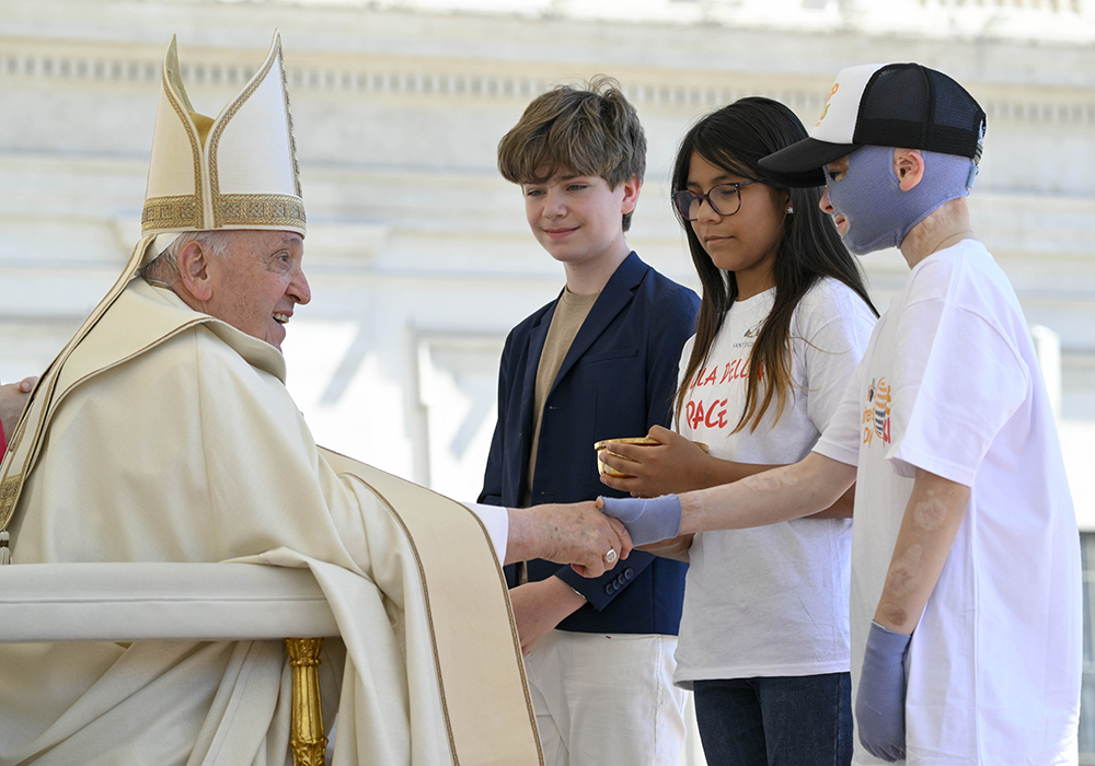 Pope Francis greets children bringing the offertory gifts during Mass in St. Peter's Square at the Vatican May 26, 2024, wrapping up the first World Children's Day held May 25-26. The pope shakes hands with Roman Oleksiv, a Ukrainian boy who lost his mother and suffered life-threatening burns from a Russian missile strike July 14, 2022. (CNS/Vatican Media)