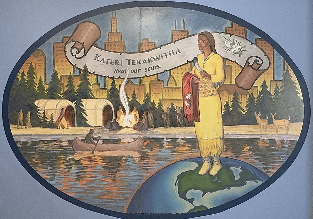 A mural of Kateri Tekakwitha, the first Indigenous North American saint, hangs in the St. Kateri Center of Chicago. In the background of the painting, created by Paul Noah, are the Chicago skyline and images depicting the Great Lakes region tribes. Though Native American families have long known about the trauma of forced assimilation, new reports have "woken up all our hearts and pains," said Jody Roy, center director. (Courtesy of Jody Roy)