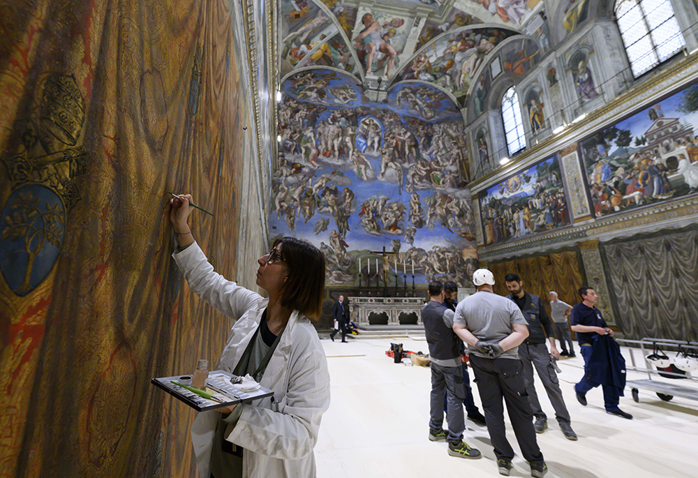As a restorer with the Vatican Museums touches up a wall fresco in the Sistine Chapel at the Vatican on May 2, 2025, workers prepare to build platforms over a protective covering on the marble floor. The cardinals who enter the conclave to elect a new pope May 7 will sit at tables facing the center of the chapel with the tables in the back row raised slightly. (CNS/Vatican Media)