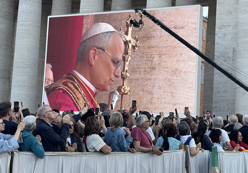 Crowds at St Peters Square greet Pope Leo XIV with their phones aloft as he stands on balcony of St. Peter's Basilica, his image appearing on a large screen, May 8 at the Vatican. (NCR photo/Rhina Guidos)